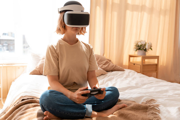 A girl enjoys the video gave via VR glasses and video game controller - Фото, изображение