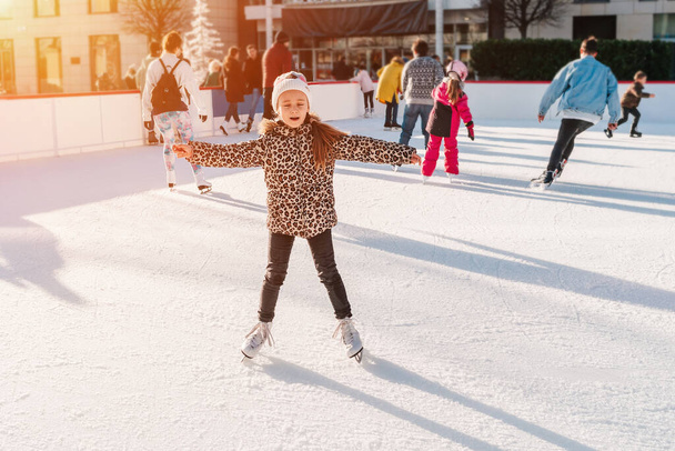 Puha, szelektív fókusz. Kis imádnivaló lány tanul korcsolyázni.Tevékenység, Felnőtt, Gyermek, Gyermekkor.Csapat tizenéves barátok jégkorcsolyázás egy jégpályán. Ünnepi és szezonális koncepció.Hobbik és szabadidő. - Fotó, kép