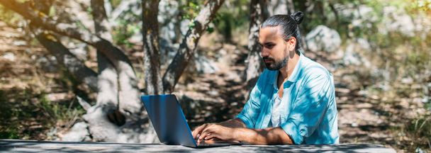 Turista masculino trabalhando em um laptop ao ar livre em um acampamento. Jovem, freelancer trabalhando online em um computador portátil em uma caminhada nas montanhas ao ar livre. A capacidade de trabalhar de qualquer lugar do mundo. - Foto, Imagem