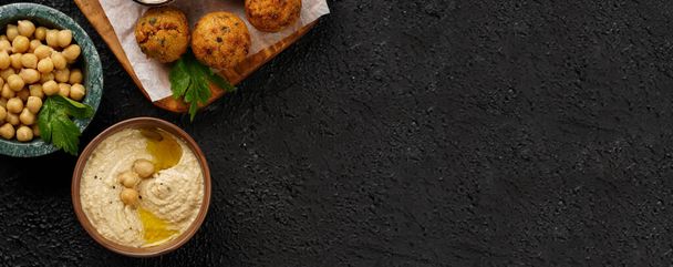 Traditional oriental chickpea deep fried falafel on a wooden board, tzatziki yoghurt sauce, hummus, fresh lime and green cilantro on black surface, copy space, banner - Foto, afbeelding