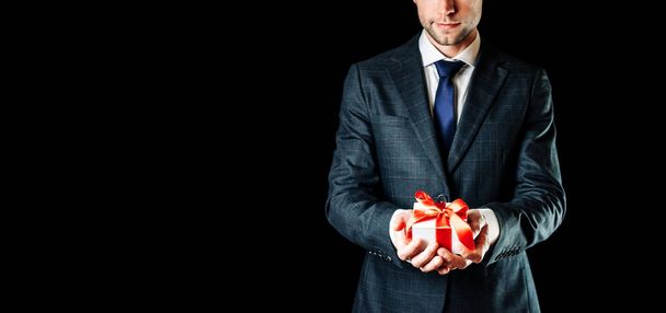 Gift man. Happy young businessman holding surprise gift box present with red ribbon isolated on black background. Black Friday, Valentine Day congratulations banner - Fotoğraf, Görsel