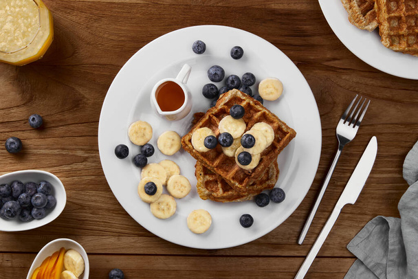 Oatmeal Belgian waffles topped with banana and blueberry on rustic wooden table. Healthy breakfast diet recipe - Photo, Image