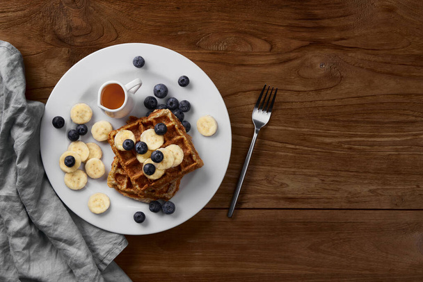 Oatmeal Belgian waffles topped with banana and blueberry on rustic wooden table. Healthy breakfast diet recipe - Foto, afbeelding