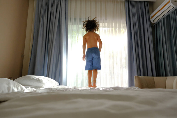 Two happy kids jumping on the bed with a phone listening to music - Fotó, kép