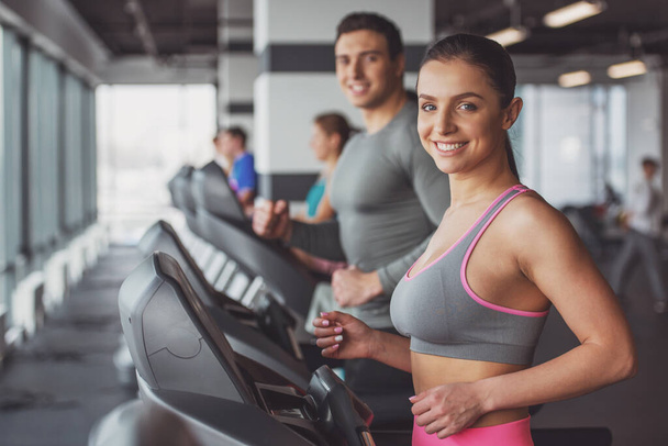 attraktive junge Frau läuft im Fitnessstudio auf einem Laufband, blickt in die Kamera und lächelt - Foto, Bild
