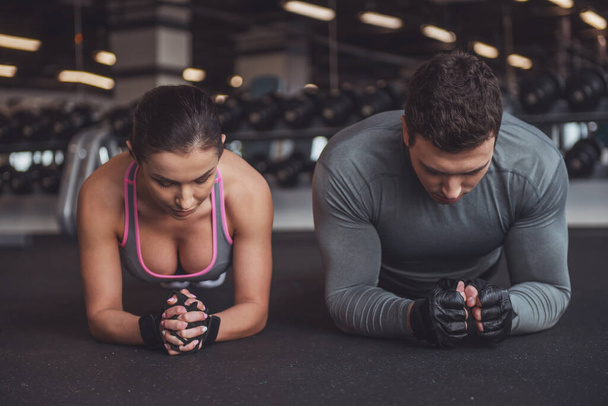 Attractive young muscular man and woman doing plank exercise while working out in gym - Fotografie, Obrázek