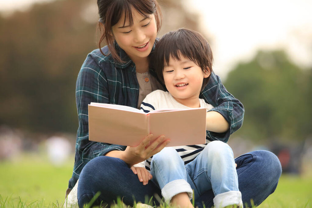 Asijské matka čtení knihy na svého syna v letním parku - Fotografie, Obrázek