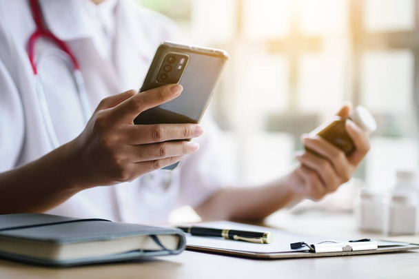Ženský lékař drží mobilní telefon a láhev léku, aby zkontroloval datum spotřeby v on-line farmaceutickém registru. - Fotografie, Obrázek