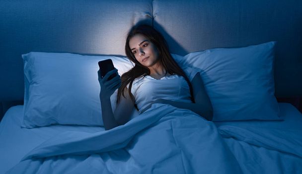 Young female using smartphone in bed at night - Foto, imagen