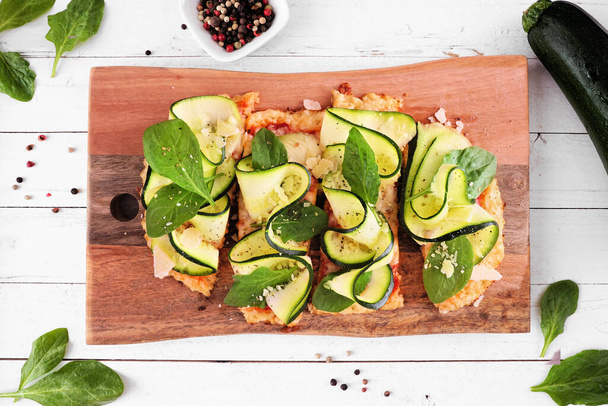 Healthy, low carb cauliflower crust flatbread with zucchini and spinach. Above view table scene on a white wood background. - Photo, Image