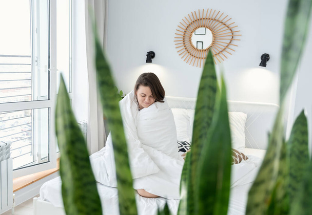 Attractive girl covered with blanket sitting on bed. Young woman enjoying morning on bed at home - Φωτογραφία, εικόνα