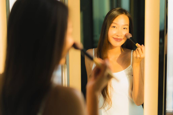 Retrato hermosa joven mujer asiática maquillaje con polvo cosmético y lápiz labial en su cara facial en el interior del baño
 - Foto, imagen