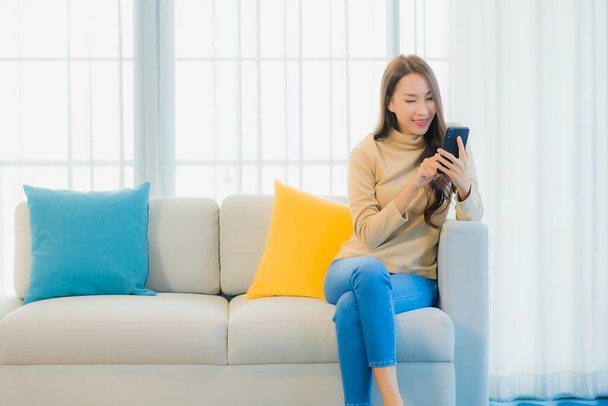 Ritratto bella giovane donna asiatica con smart cellulare sul divano in salotto interno - Foto, immagini