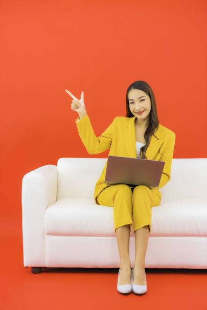 Портрет красива молода азіатка використовує комп'ютерний ноутбук на дивані з червоним тлом
 - Фото, зображення