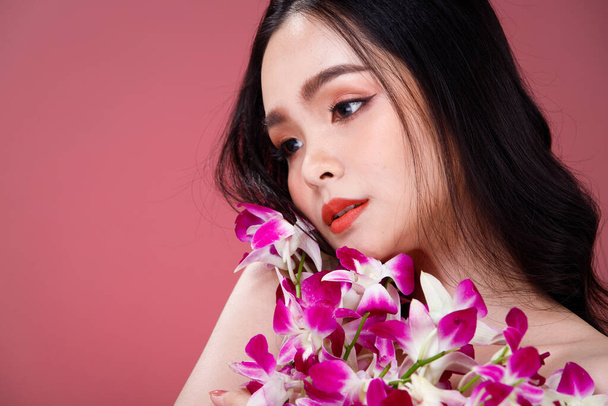 Tvář střílel Portrét módní 20s asijské ženy krásné černé vlasy vyjadřují pocit smyslný šťastný úsměv. Dívka držet fialové orchidej květiny pro péči o pleť kosmetické a ošetření přes růžové Pozadí - Fotografie, Obrázek