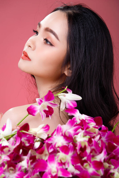 Face shot Portrait of Fashion 20s Asian Woman beautiful black hair express feeling sensual happy smile. Girl hold purple orchid flower for skin care cosmetic and treatment over pink Background - Foto, Imagem