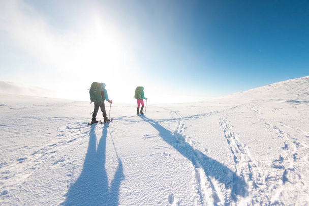 Twee vrouwen lopen in sneeuwschoenen in de sneeuw, winterwandelen, twee mensen in de bergen in de winter, wandeluitrusting - Foto, afbeelding