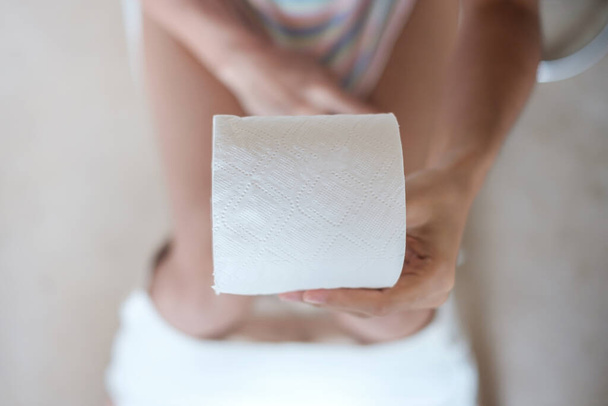 Woman holding toilet paper roll during sit on toilet bowl. diarrhea, constipated period, infection, abdominal, stomachache, cystitis, Insurance and Medical concept - Valokuva, kuva