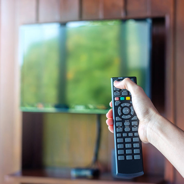 χέρι χρησιμοποιώντας τηλεχειριστήριο για να ρυθμίσετε Smart TV στο εσωτερικό του σύγχρονου δωματίου στο σπίτι ή πολυτελές ξενοδοχείο - Φωτογραφία, εικόνα