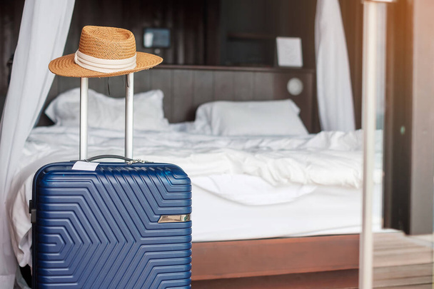 Blauwe bagage met hoed in moderne hotelkamer na de deur te openen. Tijd om te reizen, service, reis, reis, zomervakantie en vakantie concepten - Foto, afbeelding