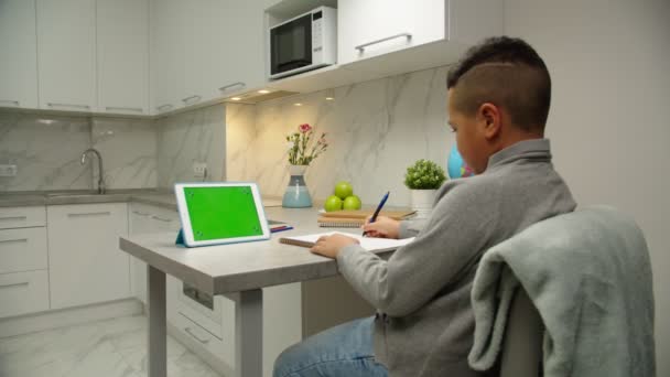 Vista posterior del niño de la escuela haciendo trabajo escolar en línea a través de la tableta en el interior - Metraje, vídeo