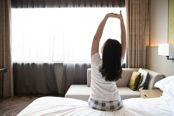 Asiatique jeune femme se réveillant du lit tôt le matin et faisant un bras étirant. - Photo, image