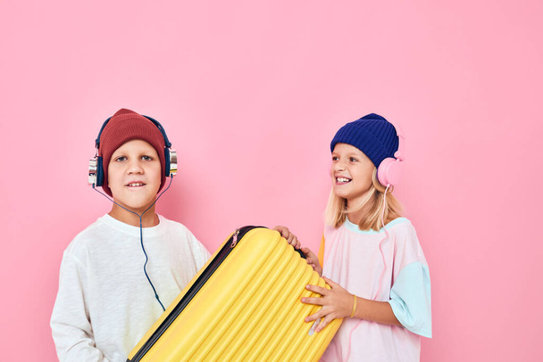 Retrato de uma menina e uma mala amarela menino com fones de ouvido Conceito de estilo de vida infantil - Foto, Imagem