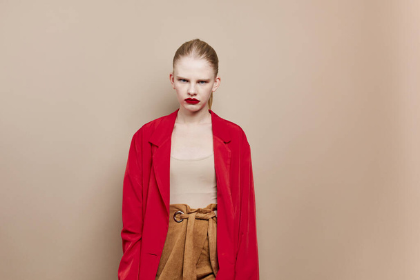 modieuze vrouw make-up in rode jas beige achtergrond - Foto, afbeelding