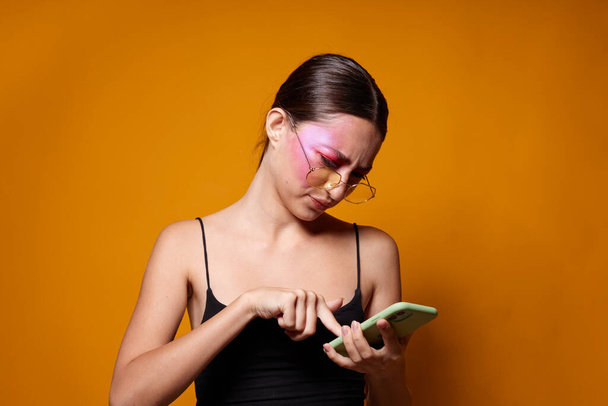 Sexy brunette woman with phone pink face makeup posing attractive look glasses yellow background unaltered - Fotó, kép