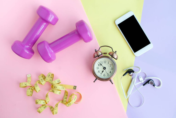 Fitnesstoestellen, Dumbbell en oortelefoon, waterflessen op een kleurrijke roze, gele en blauwe achtergrond.Health and Fitness Concepts - Foto, afbeelding