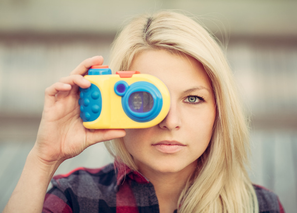 Beautiful blonde with long hair looking at the camera and holding in hands toy camera. Close up. - Fotoğraf, Görsel