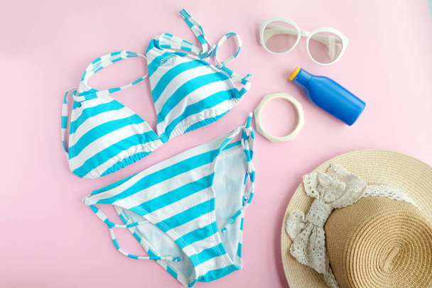 Nyári kiegészítők és kék fürdőruha bikini, Napszemüveg és kalap utazás a strandon. Rózsaszín pasztell színes háttér. Divat- és turisztikai koncepció - Fotó, kép