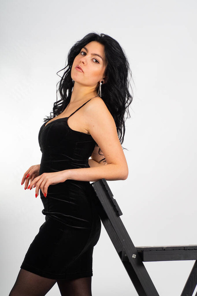 houkutteleva seksikäs nuori brunette malli yllään pieni musta mekko poseeraa kameran valkoisessa huoneessa - Valokuva, kuva