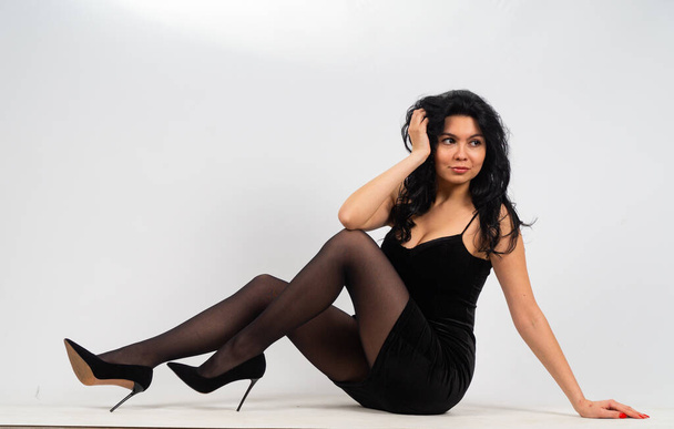 atraktivní sexy mladá brunetka model nošení v malých černých šatech pózování na kameru v bílém pokoji - Fotografie, Obrázek