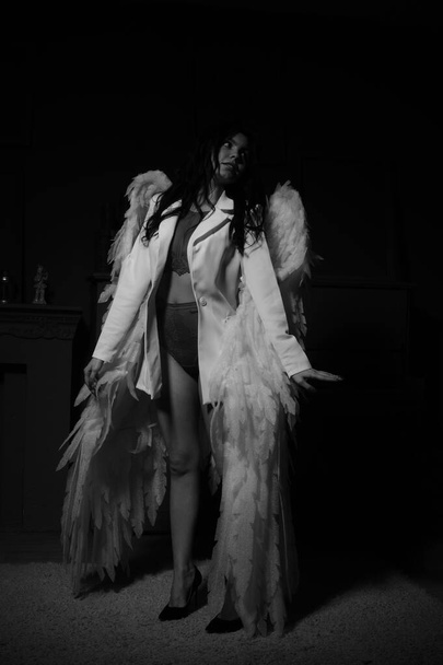 Όμορφο σέξι κορίτσι με εσώρουχα και σακάκι με φτερά που ποζάρουν στην κάμερα στο στούντιο, ασπρόμαυρη φωτογραφία - Φωτογραφία, εικόνα