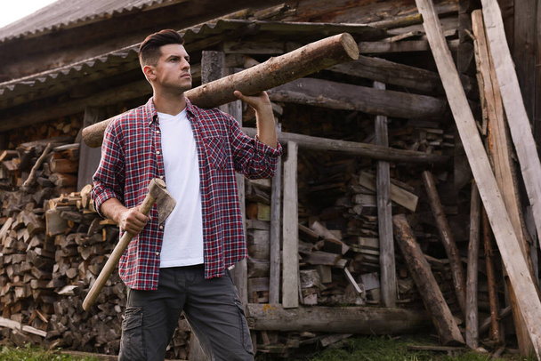 Man with ax and log near wood pile outdoors - Fotografie, Obrázek