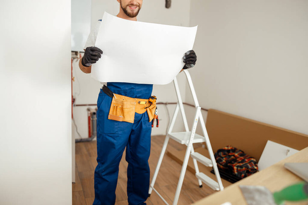 Oříznutý záběr stavebního dělníka při pohledu na nákres při stání v novém bytě - Fotografie, Obrázek
