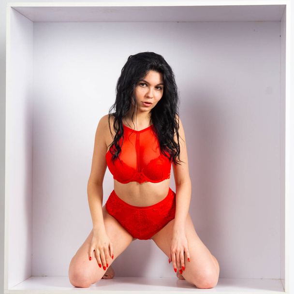 Όμορφο σέξι κορίτσι με κόκκινα εσώρουχα ποζάρουν στην κάμερα στο λευκό δωμάτιο - Φωτογραφία, εικόνα