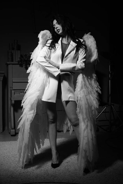 Piękna seksowna dziewczyna w bieliźnie i kurtce ze skrzydłami pozującymi do kamery w studio, zdjęcie czarno-białe - Zdjęcie, obraz