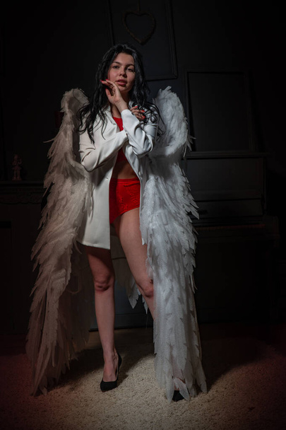 Όμορφο σέξι κορίτσι με κόκκινα εσώρουχα και λευκό σακάκι με φτερά που ποζάρουν στην κάμερα στο στούντιο  - Φωτογραφία, εικόνα