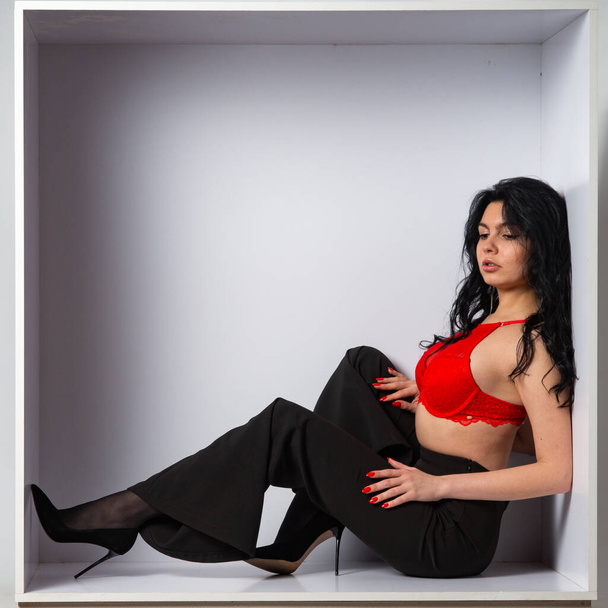 atrakcyjny sexy młody brunetka model noszenie w czerwony upraw top i czarne spodnie pozowanie przed aparatem w biały pokój - Zdjęcie, obraz
