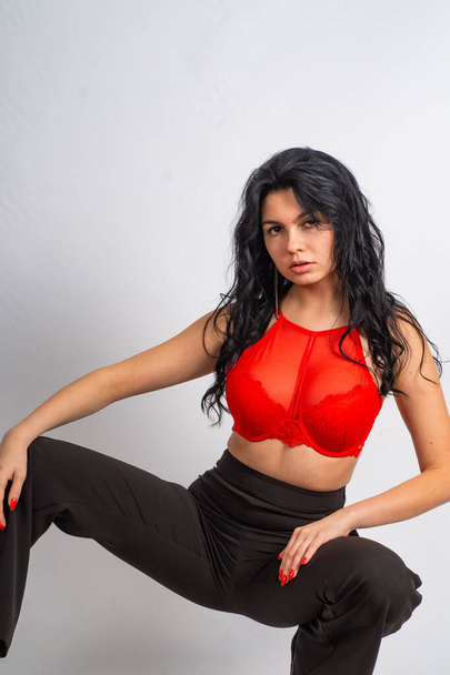 atraente sexy jovem morena modelo vestindo no vermelho cultura top e preto calças posando para a câmera no branco quarto - Foto, Imagem