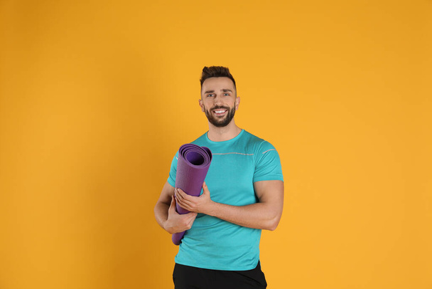 Handsome man with yoga mat on yellow background - Fotó, kép