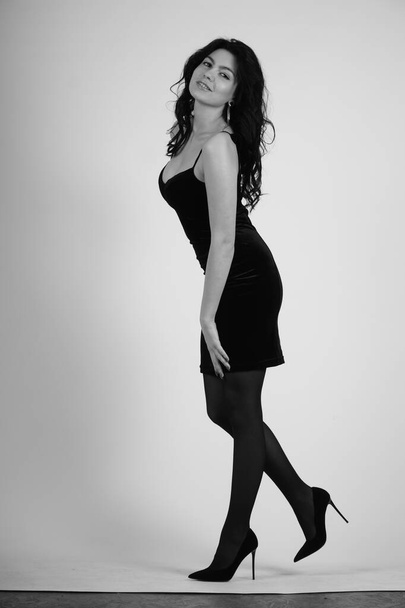 красивая молодая женщина в черном платье позирует в студии, черно-белая  - Фото, изображение