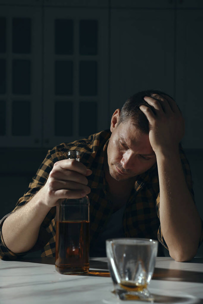 Addicted man with alcoholic drink at table in kitchen - Foto, Imagen