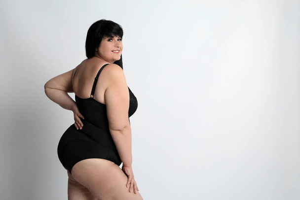 Beautiful overweight woman in black underwear on light background, space for text. Plus-size model - 写真・画像