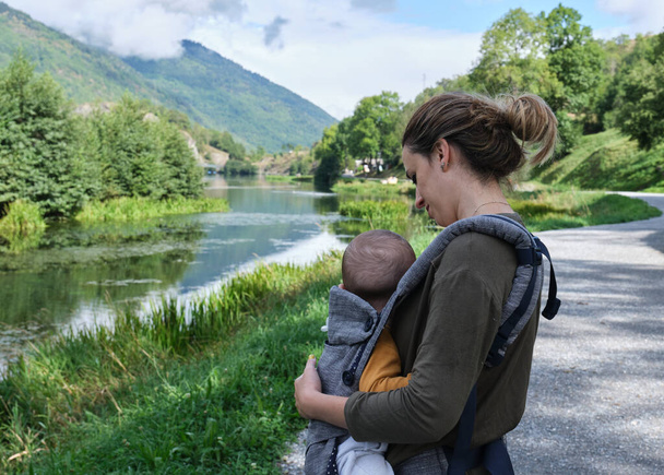 Madre caucásica con un portabebés dando un paseo por un lago en medio de la naturaleza. estilo de vida saludable - Foto, Imagen
