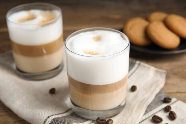 Delicious latte macchiato and coffee beans on wooden table - Foto, Imagen