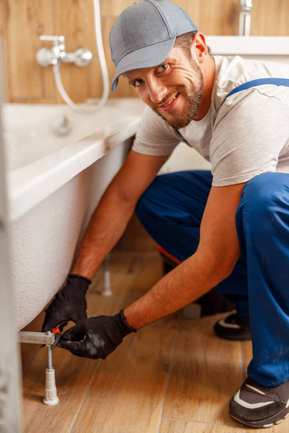 Cheerful plumber or technician smiling at camera while installing a bathtub in bathroom - Photo, Image