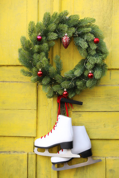 Pair of ice skates and Christmas wreath hanging on old yellow door - Φωτογραφία, εικόνα